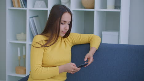 Woman-writes-messages-using-mobile-phone-sitting-on-sofa-in-living-room